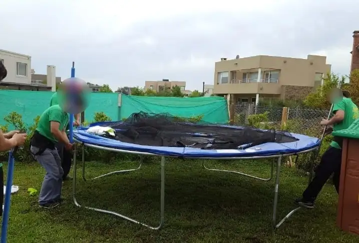 Equipo de mudanzas realizando el desarme y traslado de una cama elástica grande en el jardín de una casa en barrio privado.