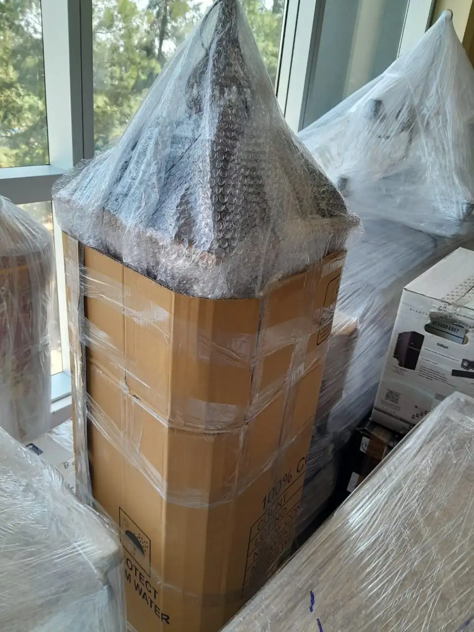 Embalaje de alta protección utilizando cartón corrugado y film para objetos altos y frágiles, garantizando seguridad en el traslado.
